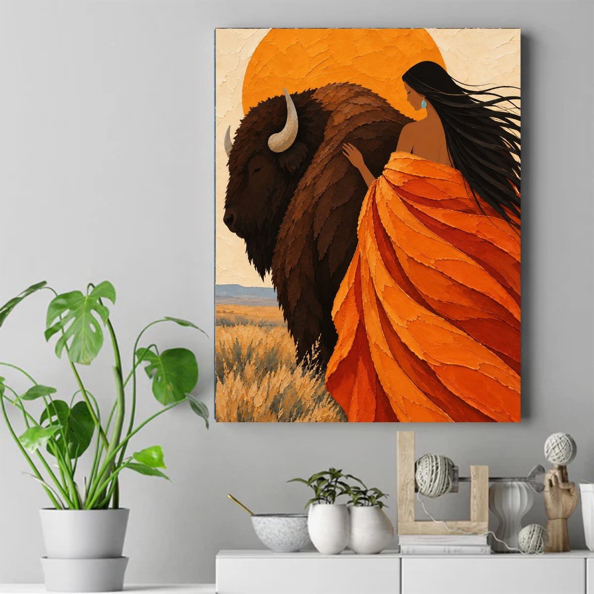 Native woman in an orange shawl resting her hand on a bison's back in front of a large orange sun and dry grass field. – ảnh 2